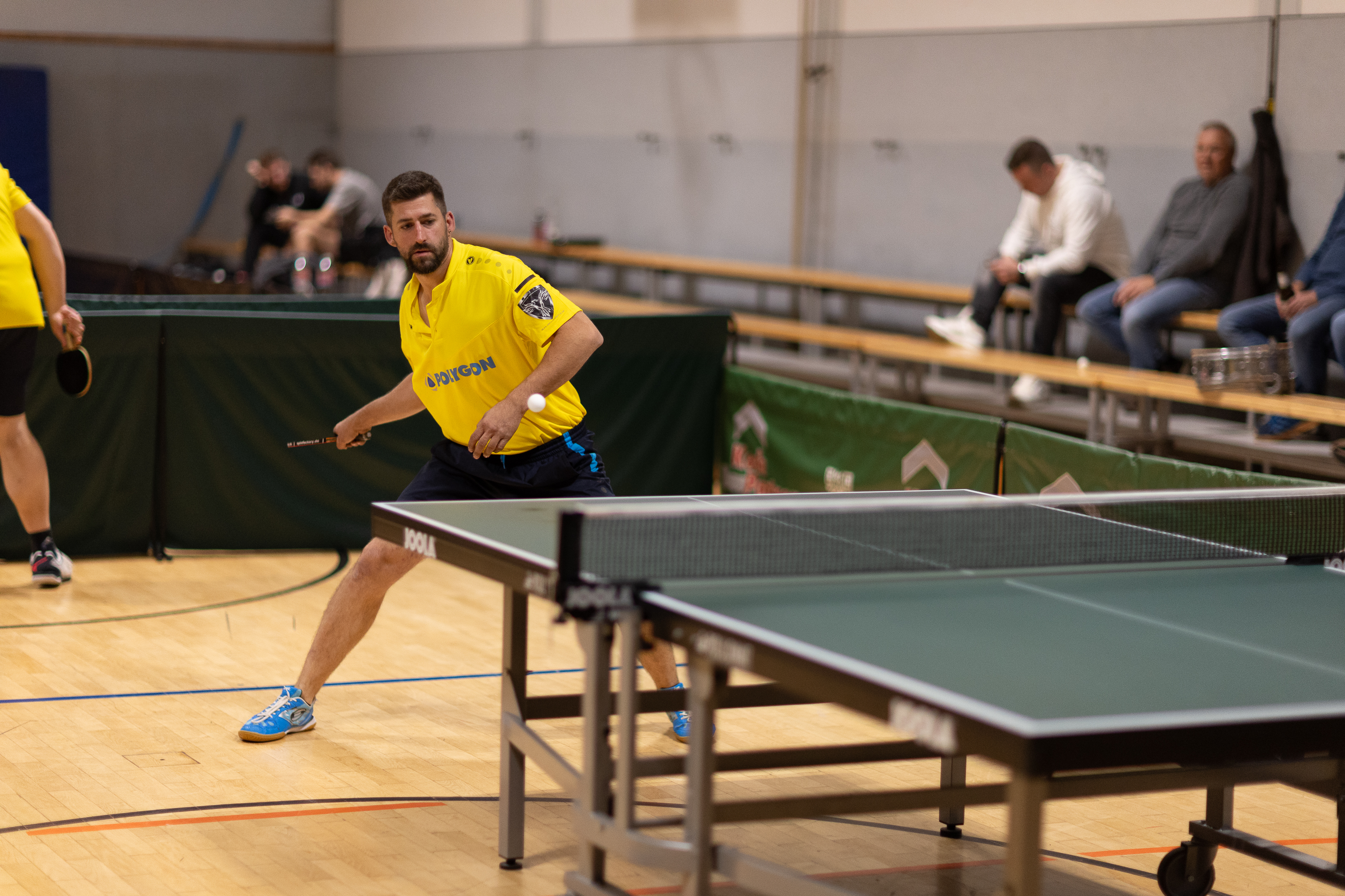Julian Buhl steht an der Tischtennis und holt zum Schlag gegen einen Tischtennisball aus.